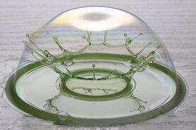 Seifenblase auf einem Tisch, wo ein Wassertropfen gerade in ihr eine Krone bildet.