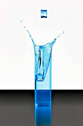 Schlankes Glas mit Wasser gefüllt. Aufnahme zeigt den Augenblick wo ein Eiswürfel ins Glas eintaucht.